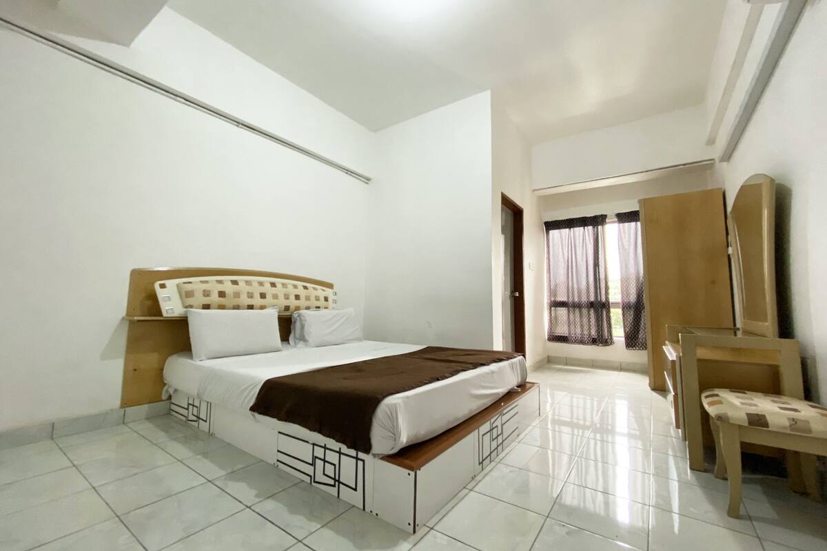 A bedroom with a bed, a chair, a wardrobe, and a window with curtains.