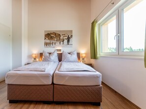 A double bed with two pillows, a wall-mounted picture, bedside lamps, and a window with curtains.