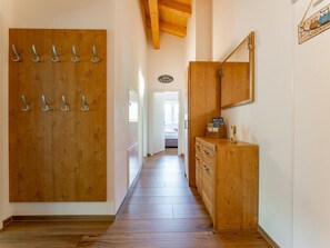 A hallway with wooden flooring, a wooden door with hooks, a cabinet with a mirror, and a sign on the wall.