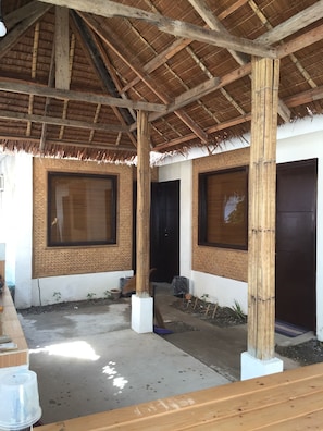 A covered outdoor area with a thatched roof, wooden pillars, and large windows. - Lolas Lodge (Boracay Island)
