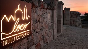 A stone wall with a neon sign for "Loco Trulli Experience" against a sunset backdrop. - Trulli residence with private pool close to Locorotondo (Puglia)