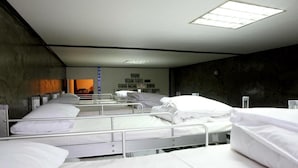 En hospitalsstue med flere senge arrangeret i rækker, hver med et privatlivs gardin og et lille natbord.