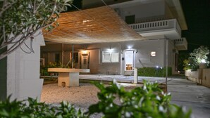 Ett modernt utomhusområde med en betongbänk, en träpergola och en gångväg som leder till en byggnadsingång.