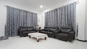 A living room with two leather sofas, a coffee table, and grey curtains. - OYO 90203 Emma Sukma Homestay (Kuching)