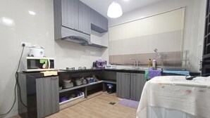A compact kitchen with a microwave, stove, and sink. There is a window with blinds, a small trash bin, and a shelf with dishes. - OYO 90203 Emma Sukma Homestay (Kuching)