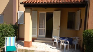 A covered outdoor seating area with a table and chairs, a small covered entrance, and a tiled roof. - Delta Blu Residence Village - Villetta Trilocale 05 (Lido di Pomposa)