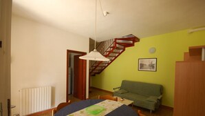 A dining area with a table, chairs, a green sofa, a staircase, and a radiator. - Delta Blu Residence Village - Villetta Trilocale 05 (Lido di Pomposa)