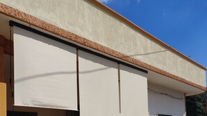 Un edificio con fachada color beige, toldo blanco y una cerca decorativa.