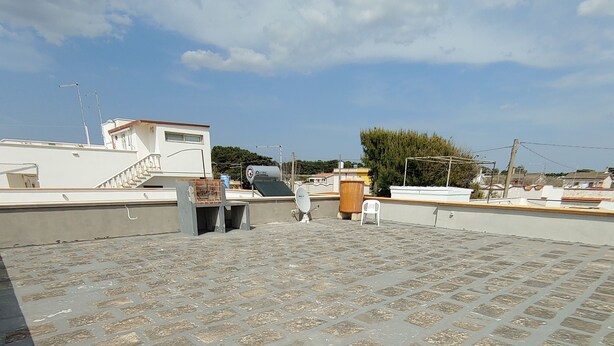 Una terraza en la azotea con suelo de baldosas, una antena parabólica y una silla blanca.