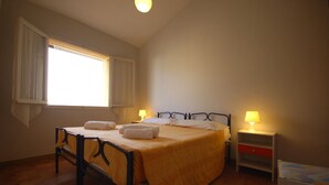 A bedroom with a bed, two bedside tables with lamps, a window with curtains, and a wooden floor. - Delta Blu Residence Village - Villetta Trilocale 16 (Lido di Pomposa)