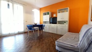 Ein Wohnzimmer mit einer Couch, einem Esstisch mit Stühlen, einem Fernseher und Schränken.