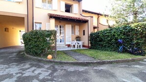 Ein zweigeschossiges Haus mit einer Terrasse, die einen Tisch, Stühle, ein Fahrrad und einen gepflegten Rasen zeigt.