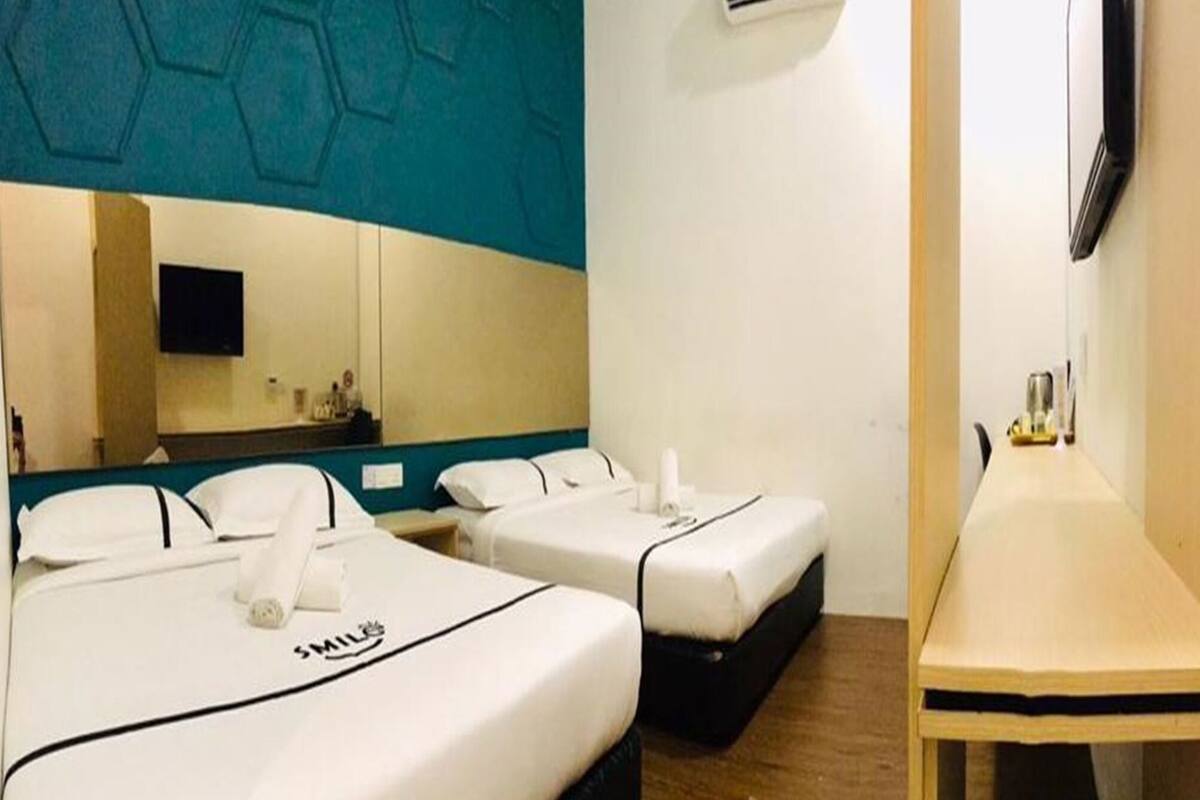 Une chambre d’hôtel avec deux lits, une petite table, un miroir et un téléviseur.