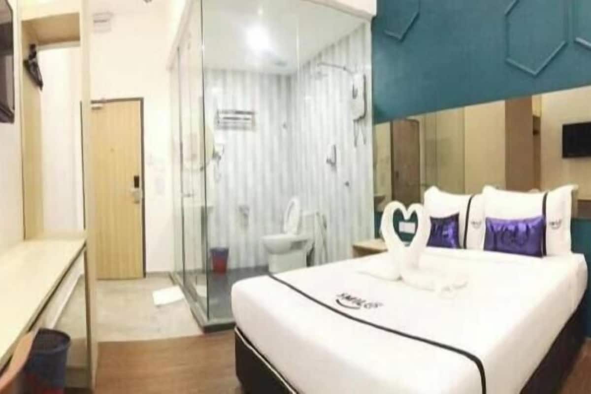 Une chambre d’hôtel comprenant un lit, un bureau, une cloison en verre et un espace douche.