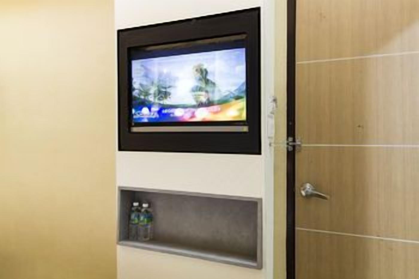 A television mounted on a wall with a shelf below it containing a bottle and a small item.