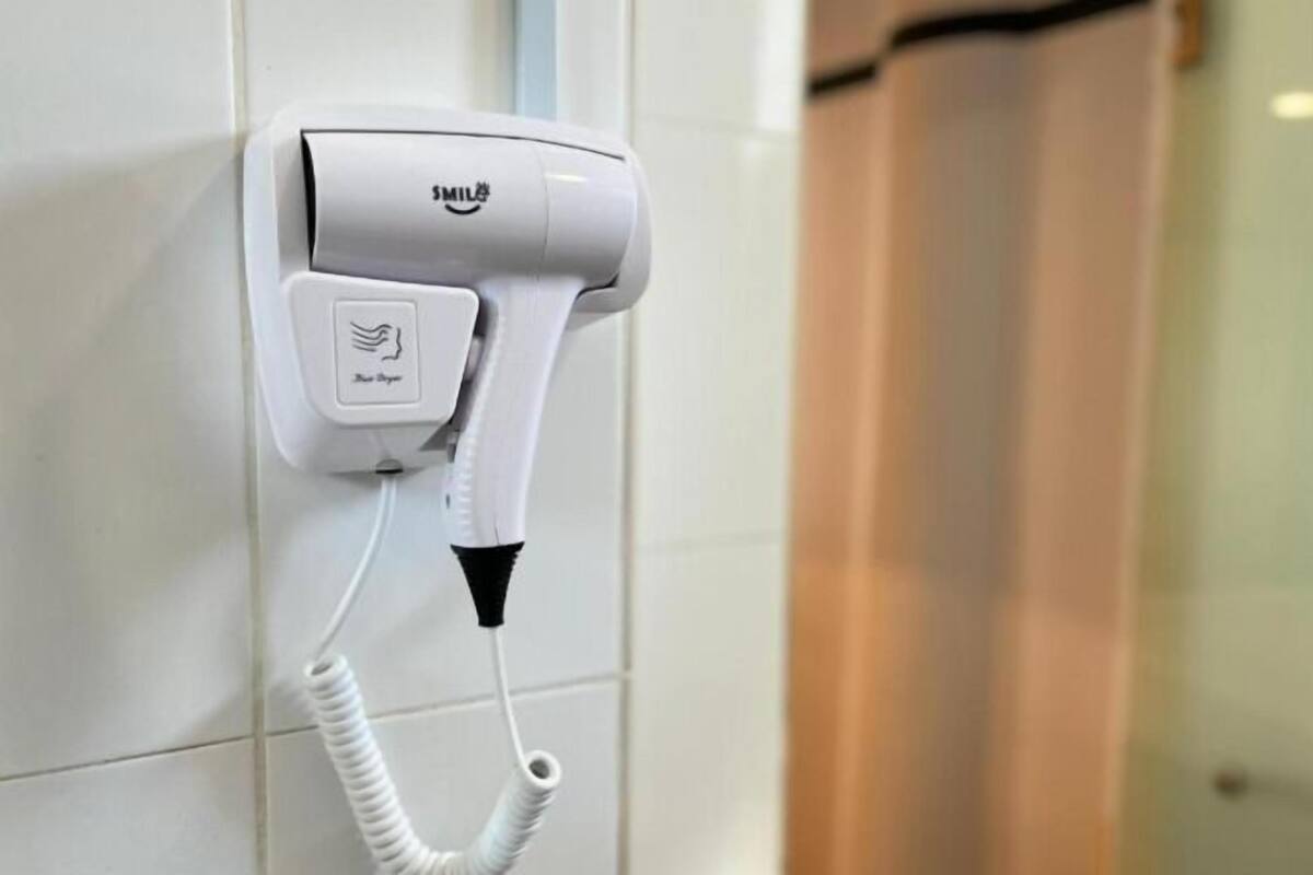 Un sèche-cheveux fixé au mur, doté d’un cordon, d’une prise de courant et d’un panneau de commande avec un symbole représentant une main.