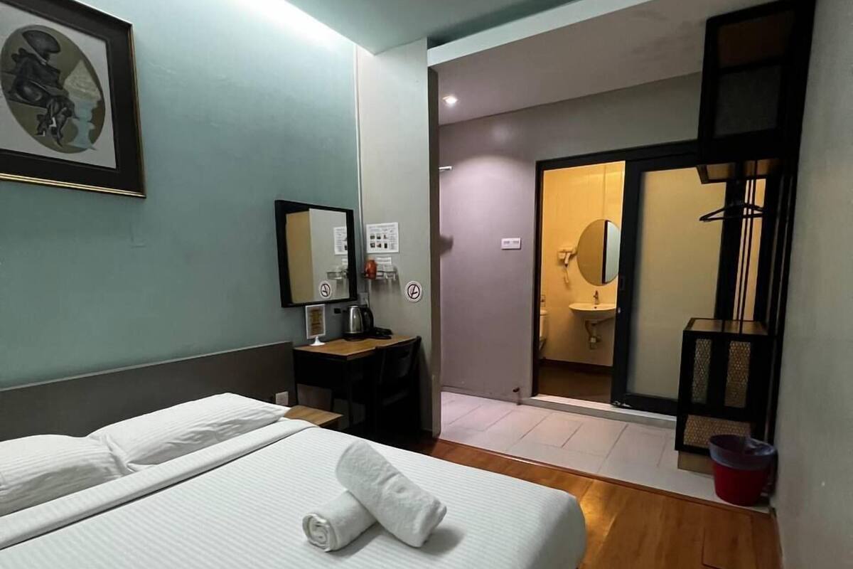 Une chambre d’hôtel avec un lit, un bureau, un miroir et une salle de bain visible à travers une porte ouverte.