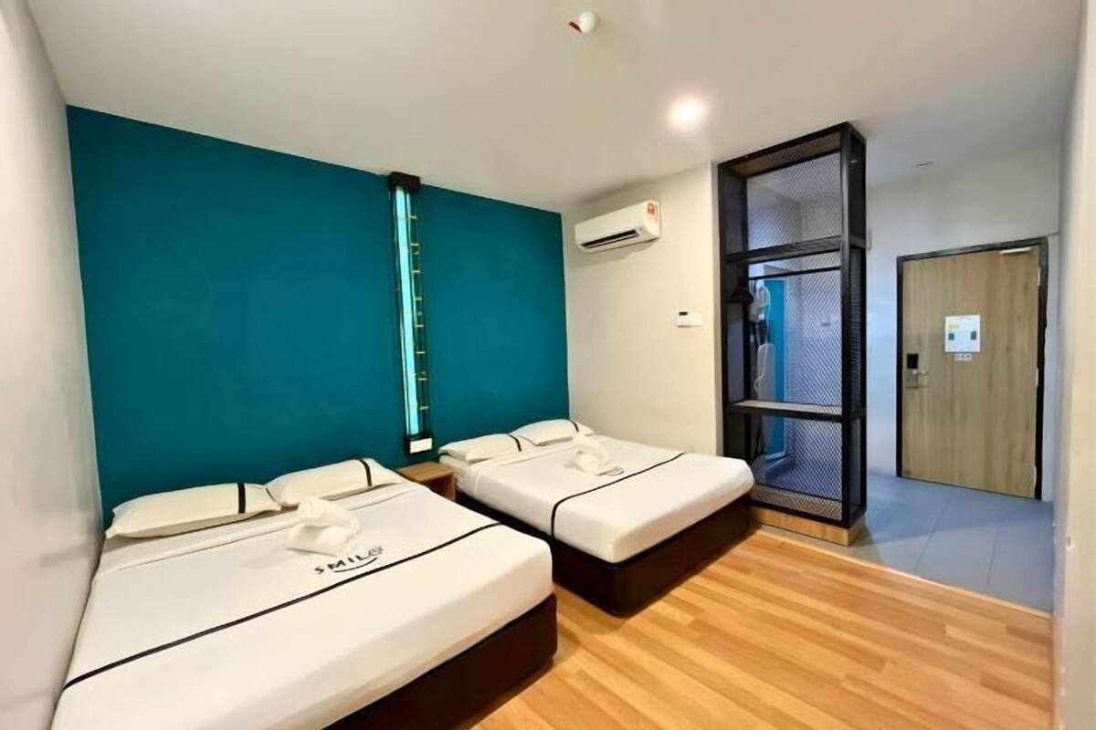 Une chambre avec deux lits, des murs de couleur turquoise, un plancher en bois, un appareil de climatisation et une porte-moustiquaire.