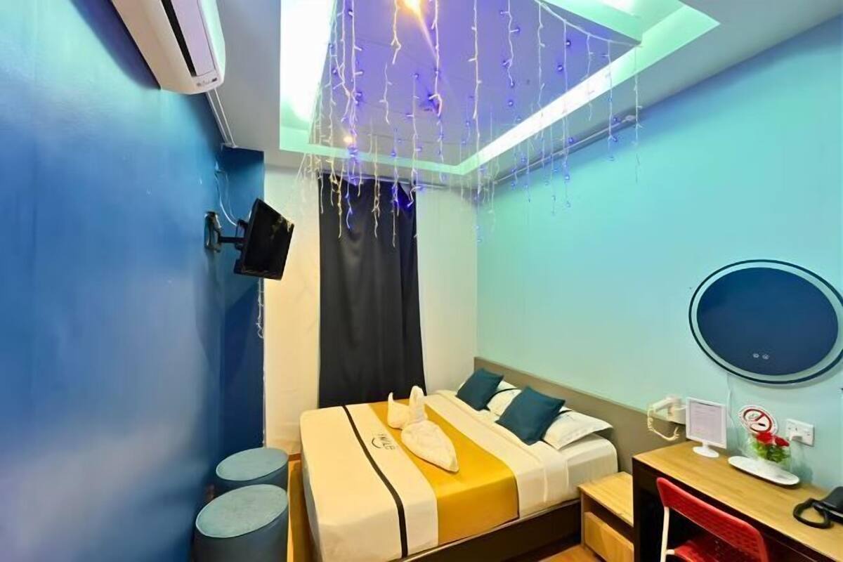 Une chambre d’hôtel équipée d’un lit, d’une table de chevet, d’un bureau, d’une chaise, d’un climatiseur et d’un luminaire au plafond.