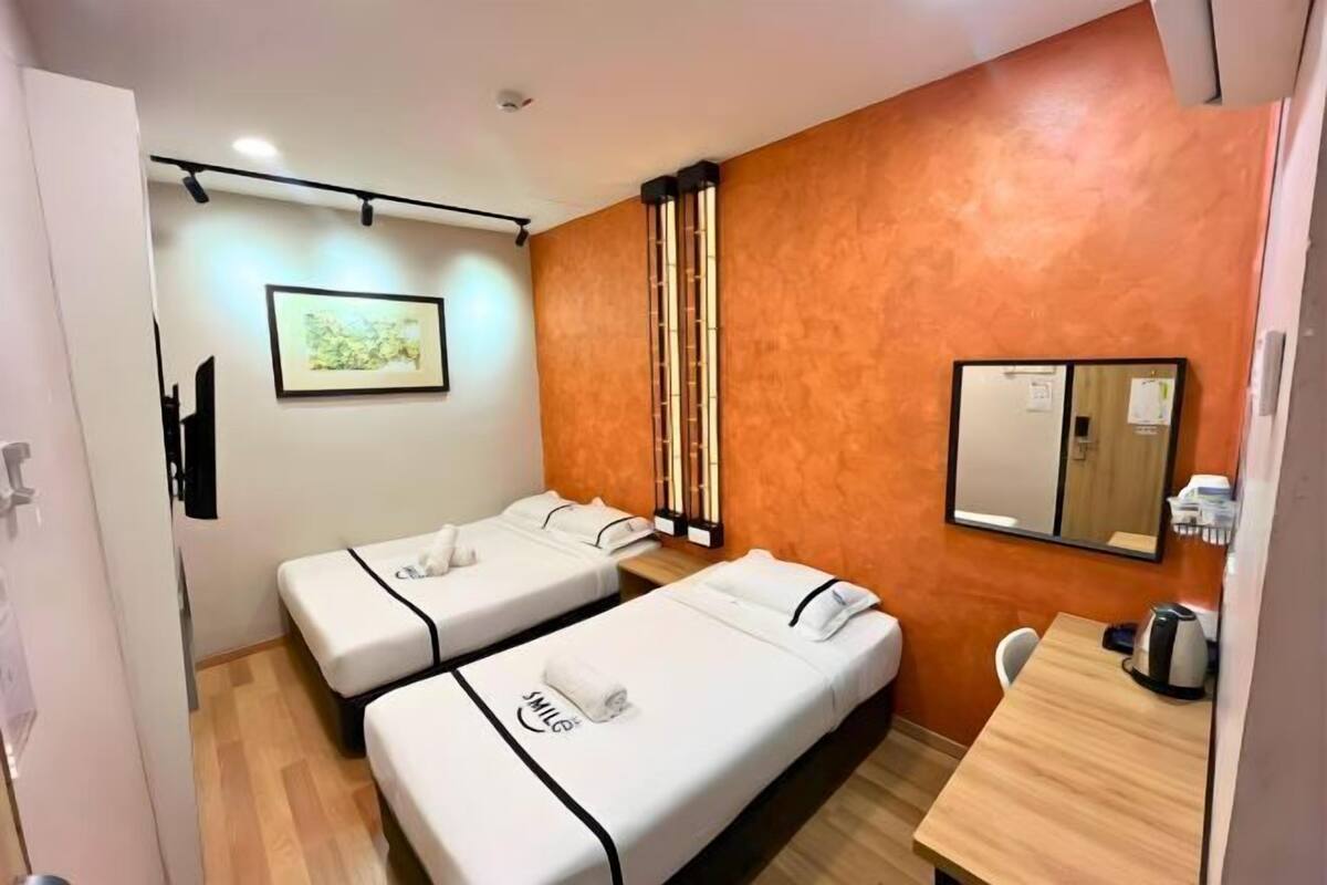 Une chambre d’hôtel avec deux lits simples, une table en bois, un miroir et un tableau encadré au mur.