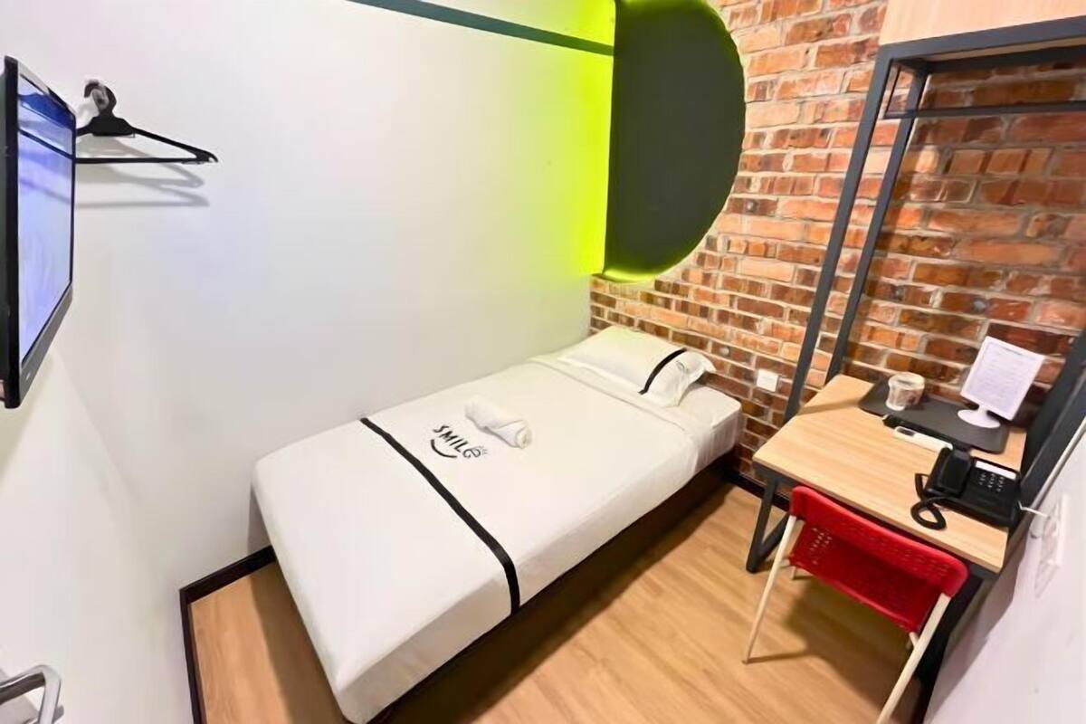 Une petite chambre d’hôtel comprenant un lit, un bureau, une chaise, un miroir et un téléviseur.