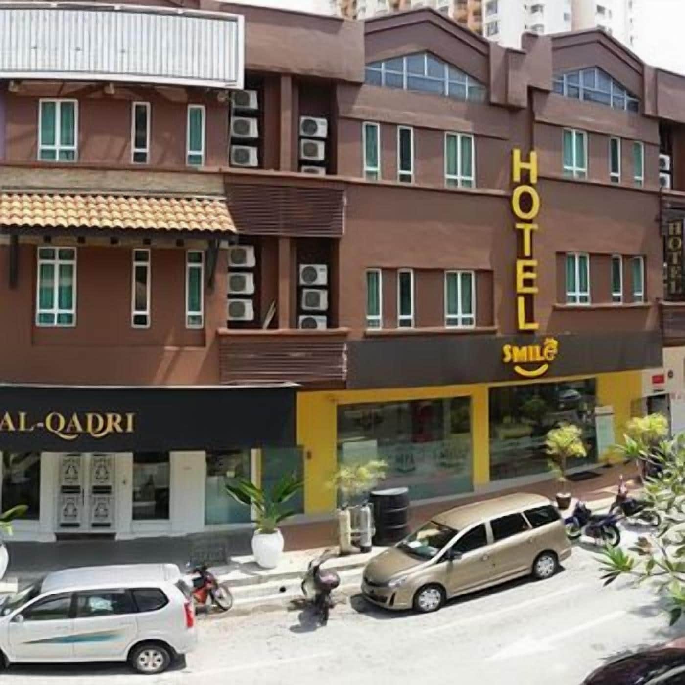 A hotel with multiple floors, a sign reading 'HOTEL SMILE,' and a storefront with 'AL-QADRI' signage.