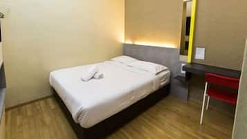A small, neatly made bed with a white duvet and a single pillow, a wooden floor, a small bedside table with a red chair, and a mirror on the wall.
