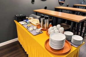 Un buffet avec une table jaune, des assiettes, des tasses et une cafetière.