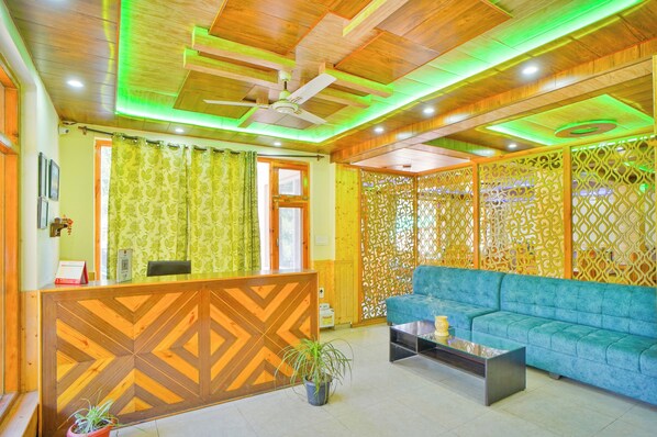 Un área de recepción con un mostrador de madera, un sofá azul, un ventilador de techo y un separador decorativo.