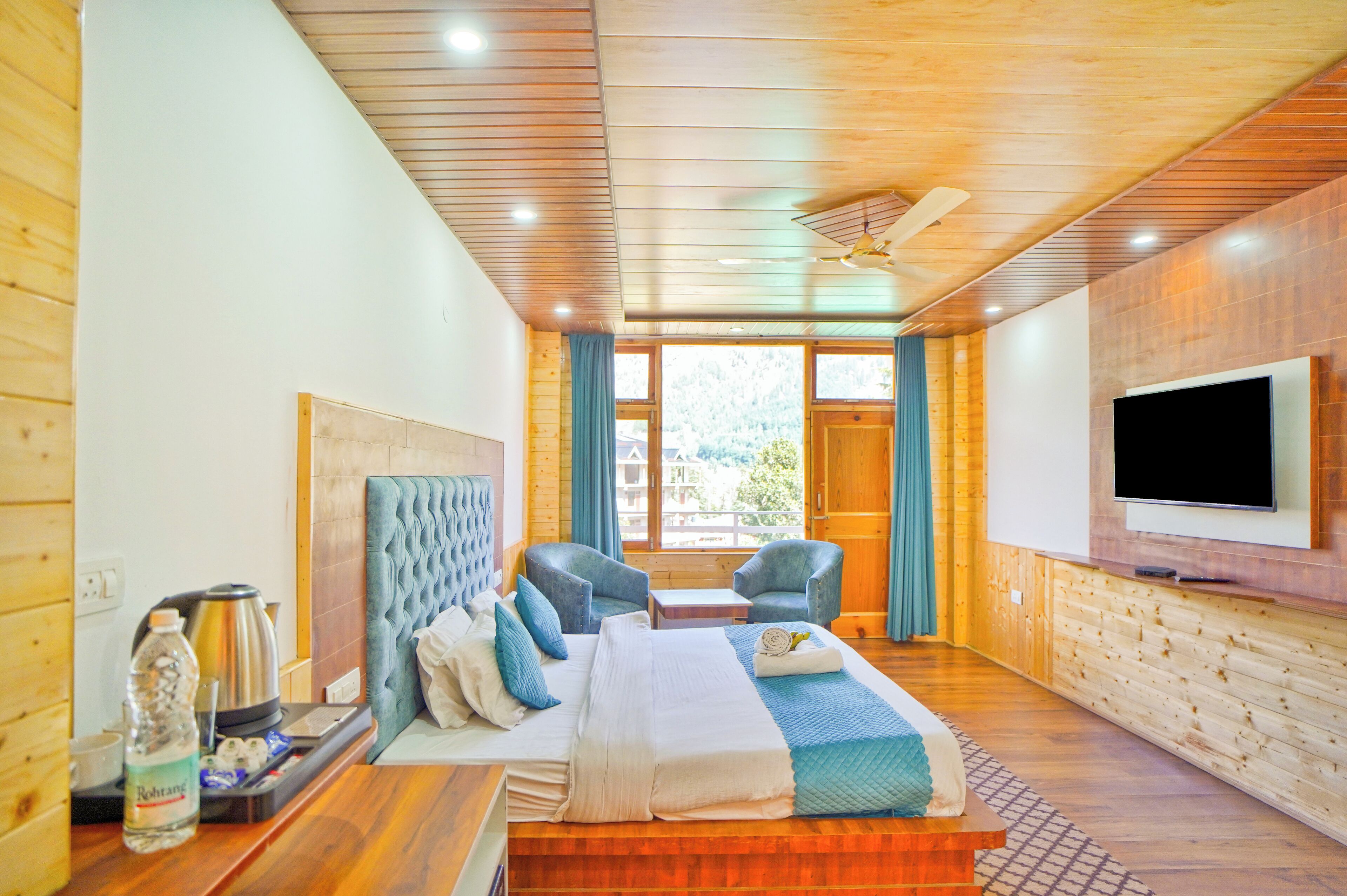 A hotel room with a bed, two chairs, a TV, and a window with curtains.