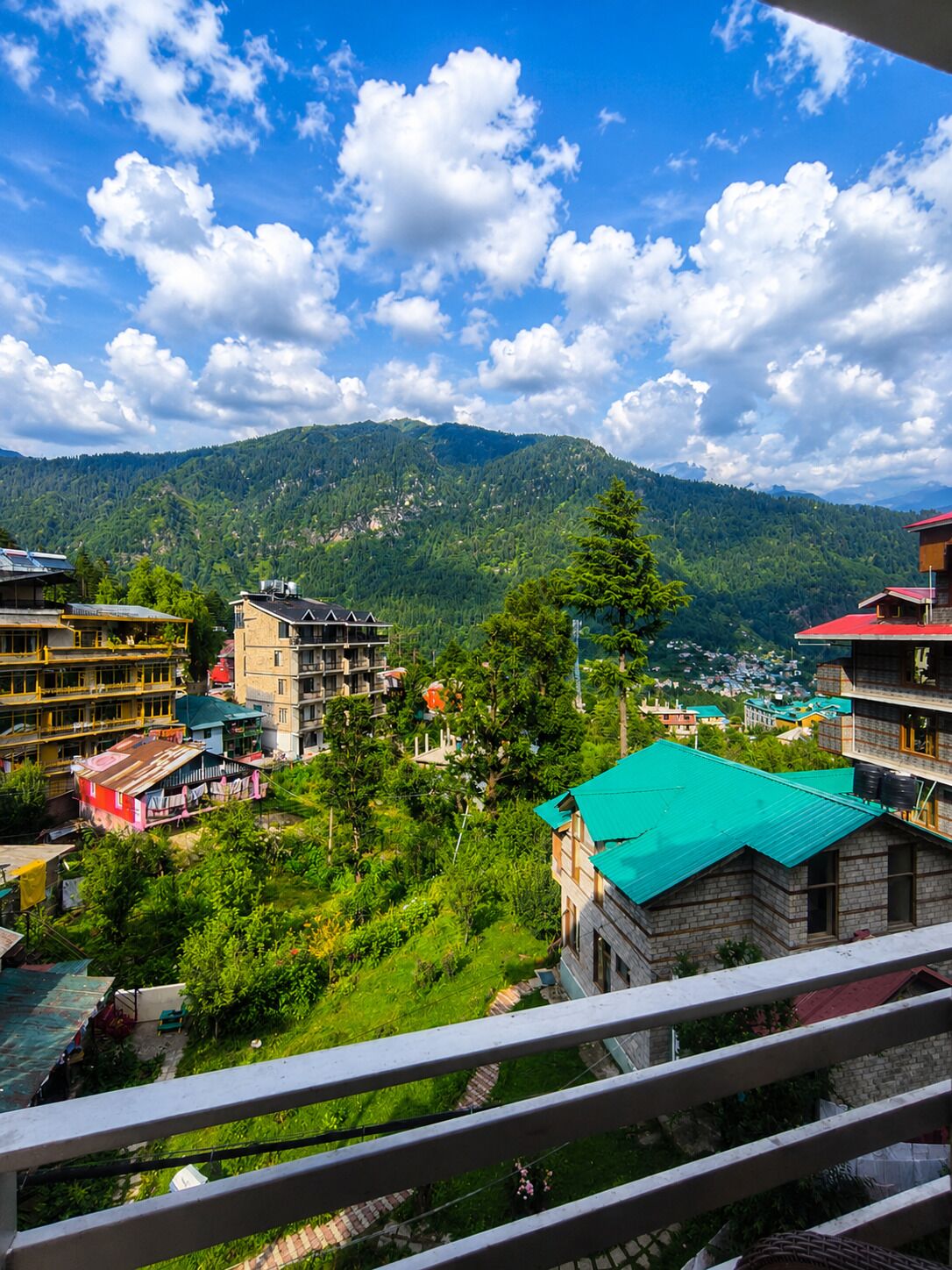 A mountainous landscape with buildings, including a multi-story structure with a green roof and a smaller building with a red roof.