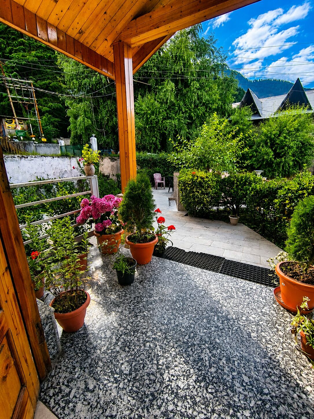 A covered outdoor area with potted plants, a wooden pergola, and a view of a mountainous landscape.