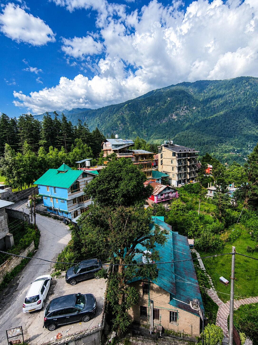 Un village de montagne où se côtoient des bâtiments traditionnels et modernes, avec une route pavée et des voitures garées.