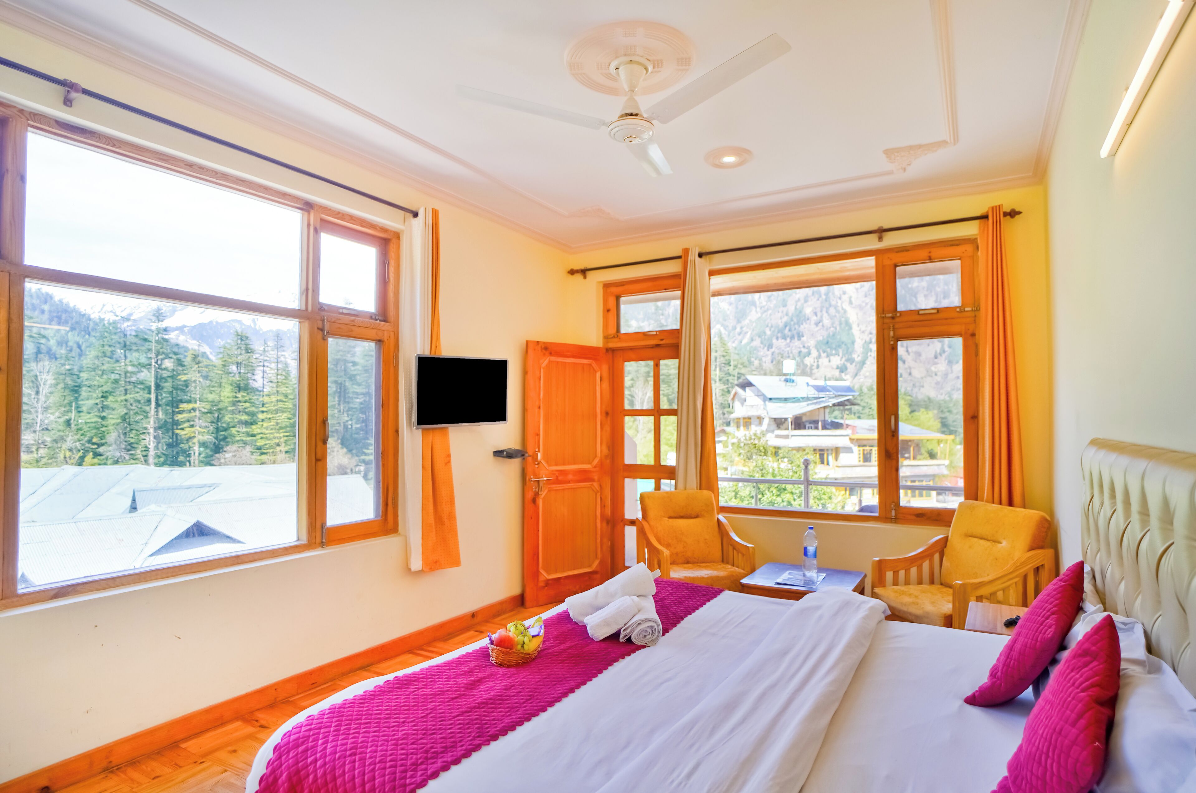 A hotel room with a large bed, a television, a chair, and a window with a mountain view.