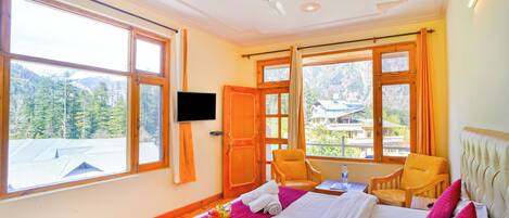 A hotel room with a large bed, a television, a chair, and a window with a mountain view.
