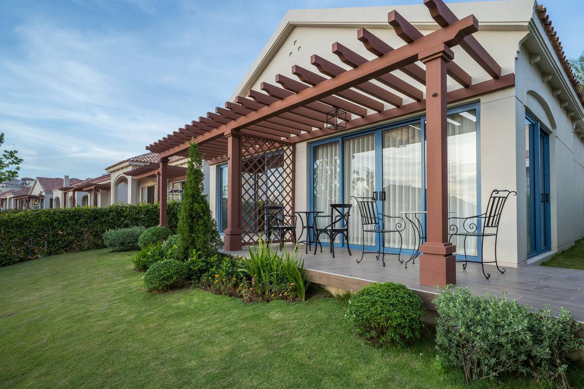 A covered patio with outdoor furniture, a well-maintained lawn, and a building with large windows and a pergola.