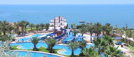 Un resort con una gran piscina, palmeras y vista al océano.