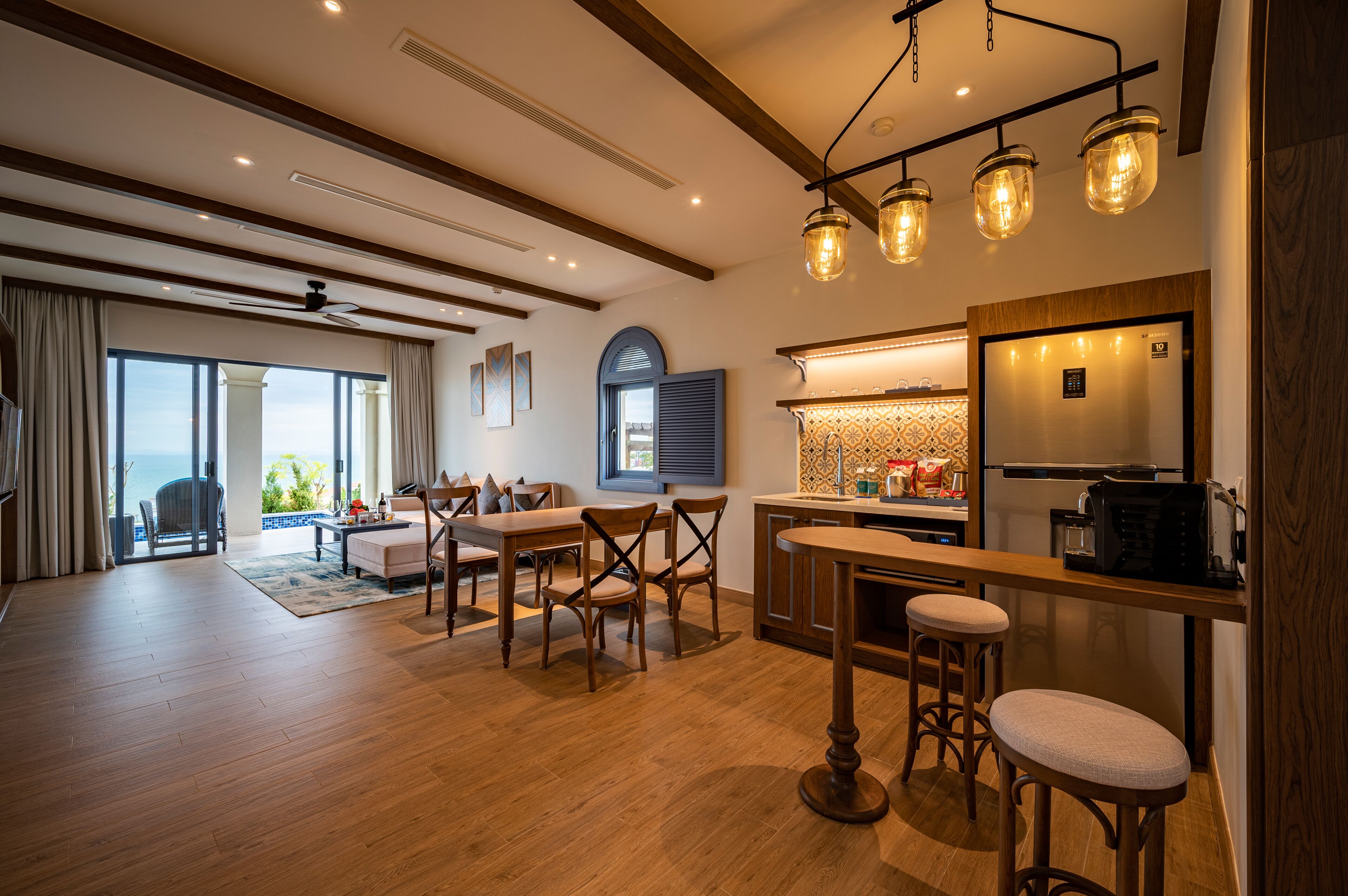 Een ruime woonkamer met houten vloer, een eettafel met stoelen, een keuken met een koelkast, en een bar met krukken.