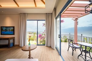 A balcony with a view of the sea, a table with chairs, and a TV on the wall.