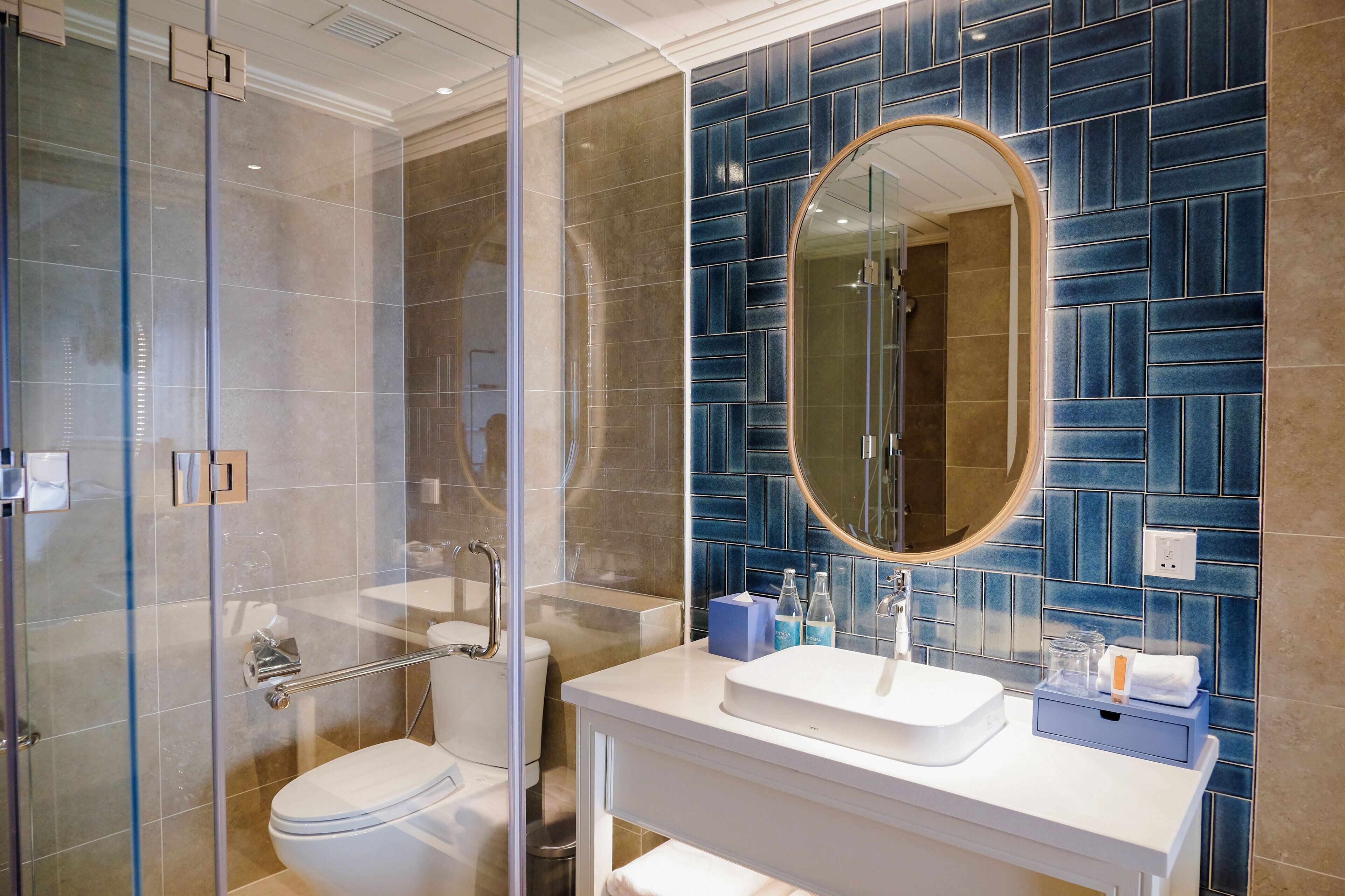 A modern bathroom with a glass shower enclosure, a white sink, and a blue-tiled wall.