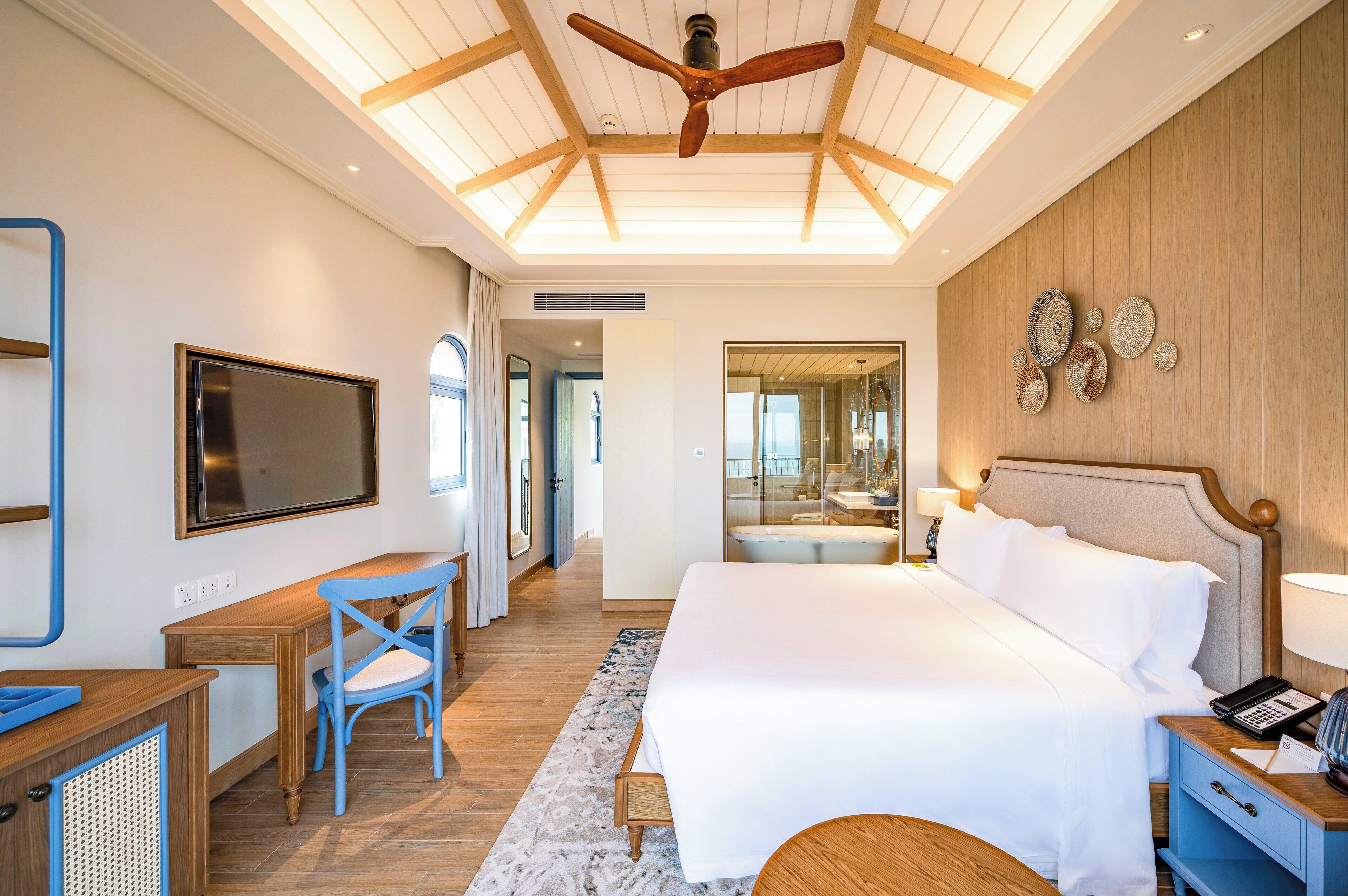 Una habitación de hotel moderna con una cama grande, un escritorio con silla, un televisor y un ventilador de techo.