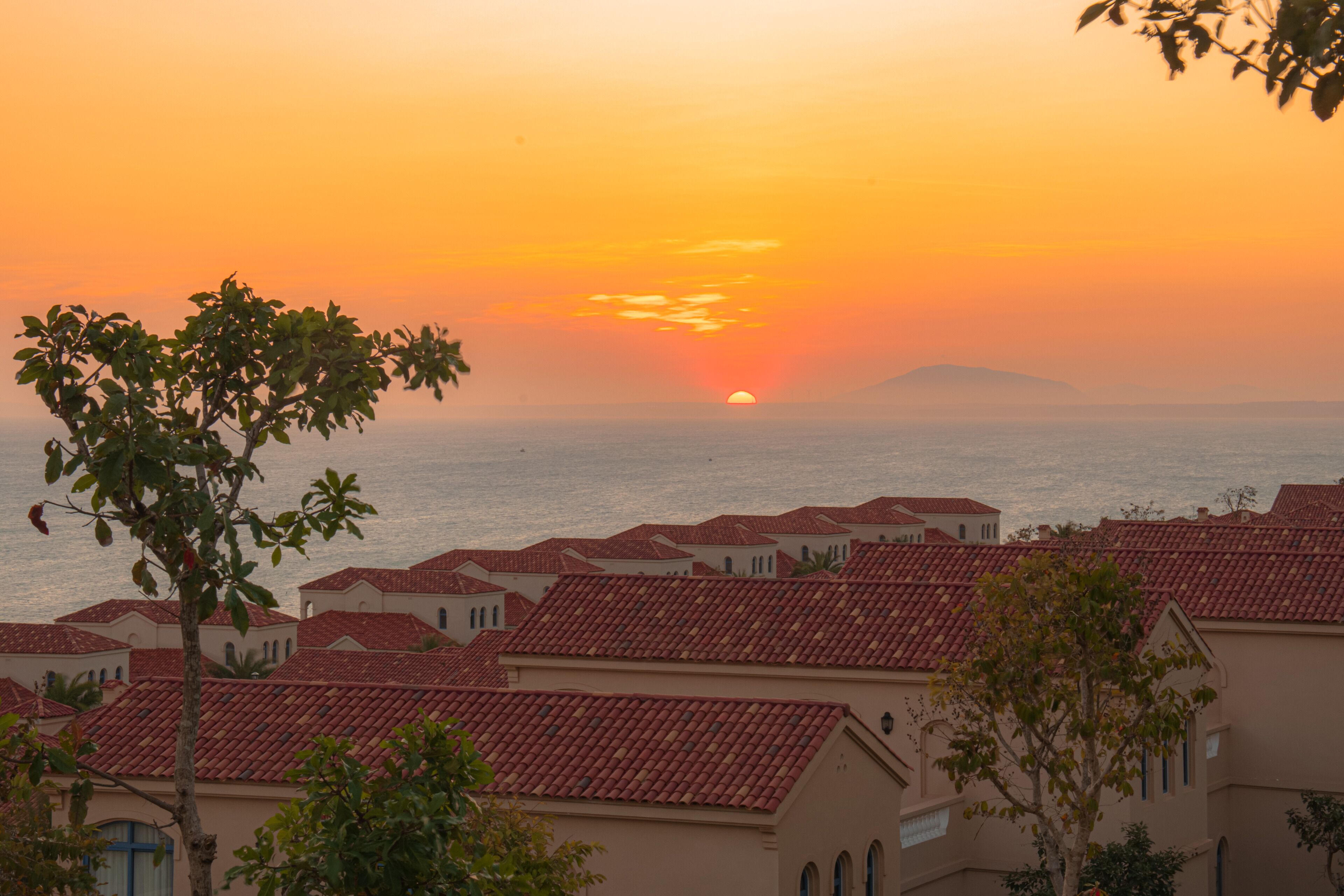 Un pueblo costero con tejados rojos y un atardecer sobre el mar.