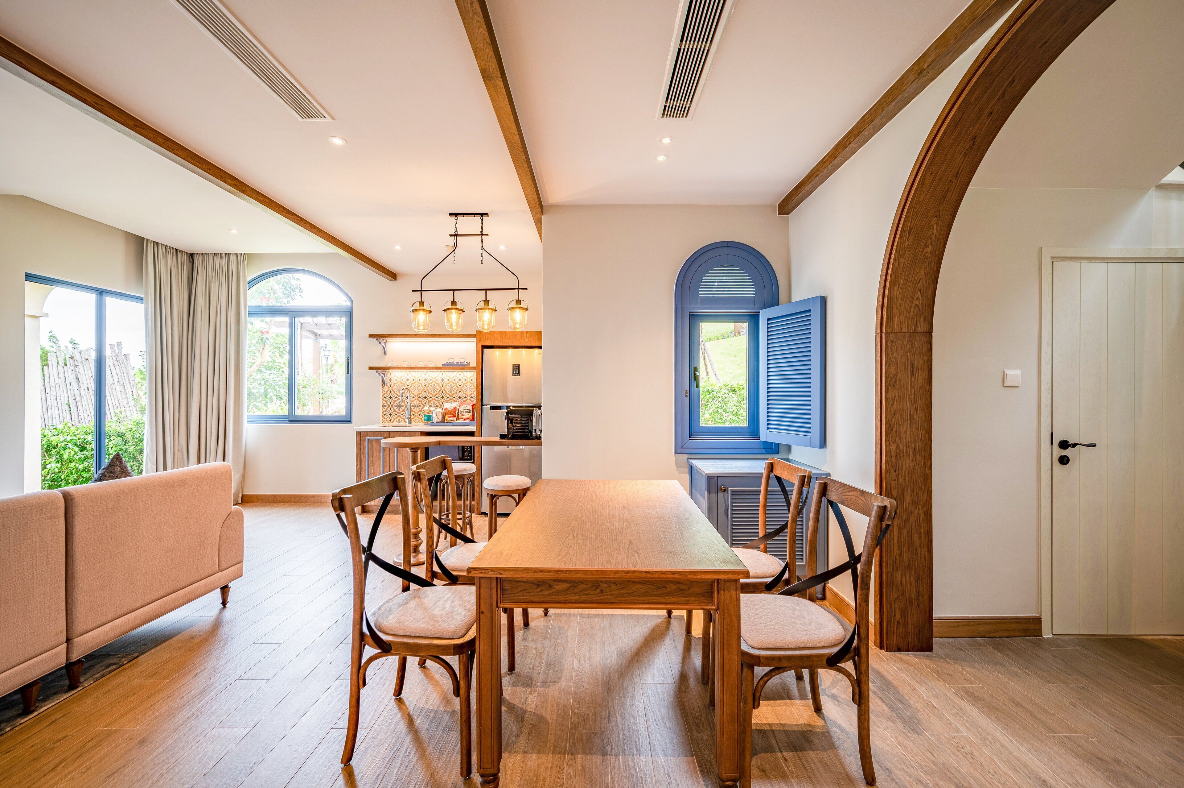 Un comedor con una mesa y sillas de madera, un sofá y una cocina al fondo.