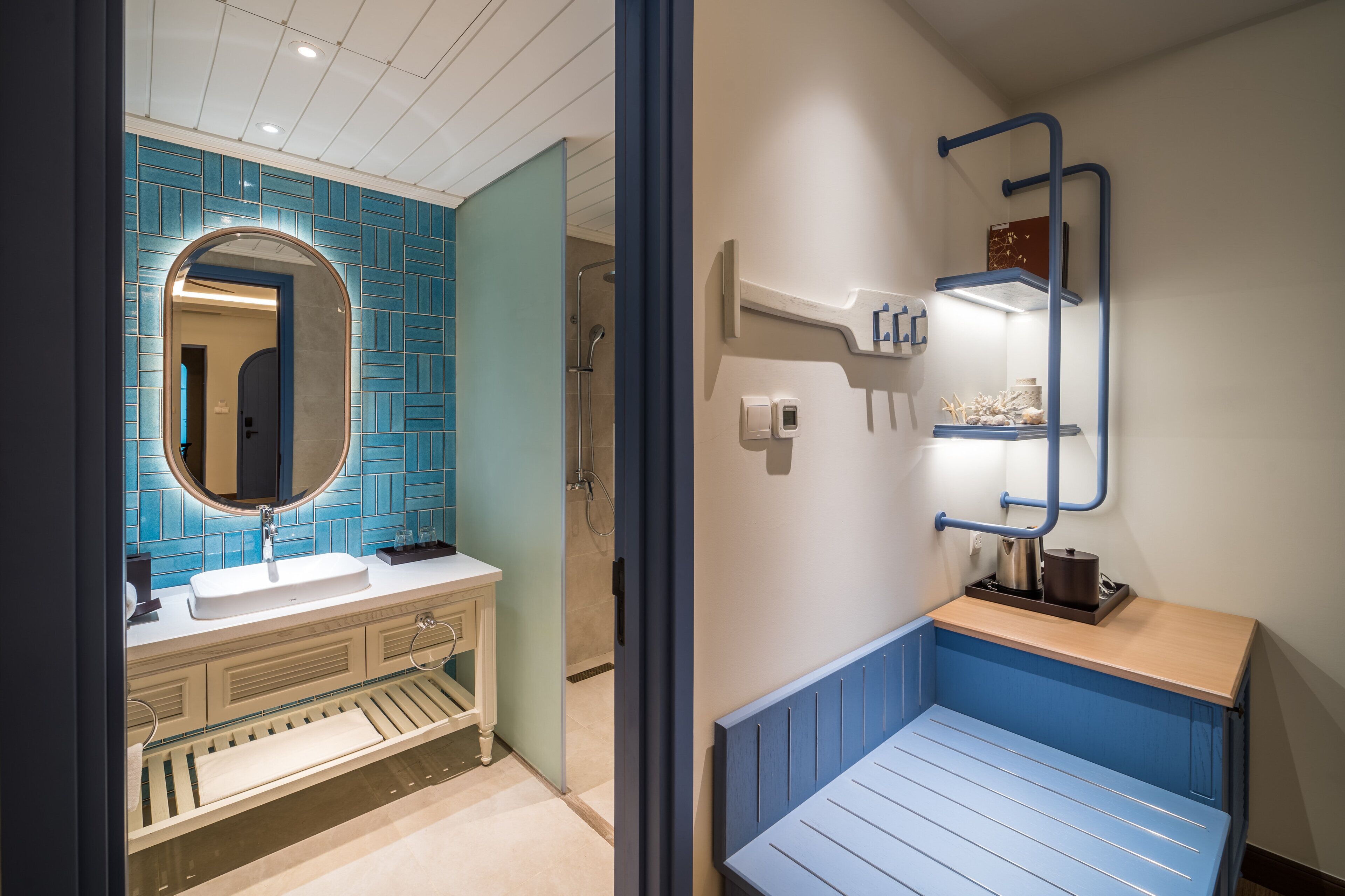 A modern bathroom with a blue tiled wall, a round mirror, a white sink, and a blue bench.