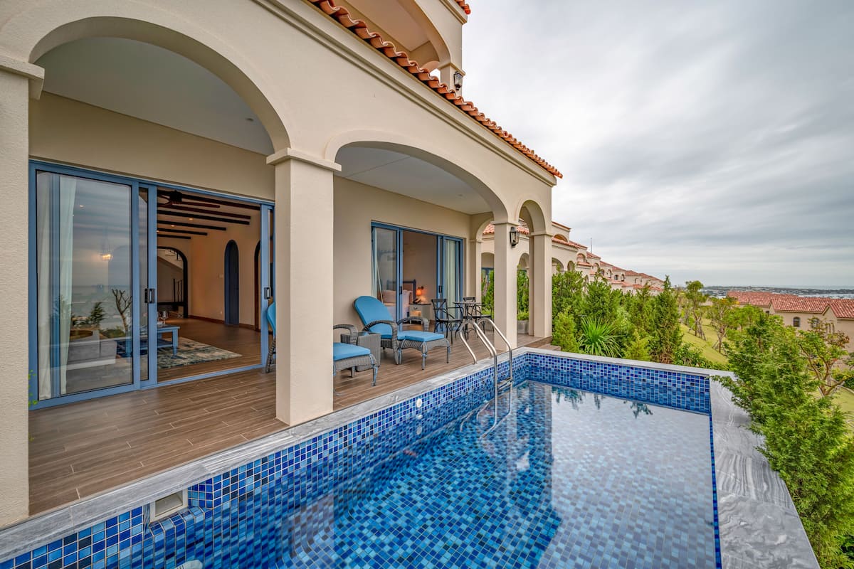 A modern outdoor pool area with a wooden deck, blue-tiled pool, and a view of the surrounding landscape.