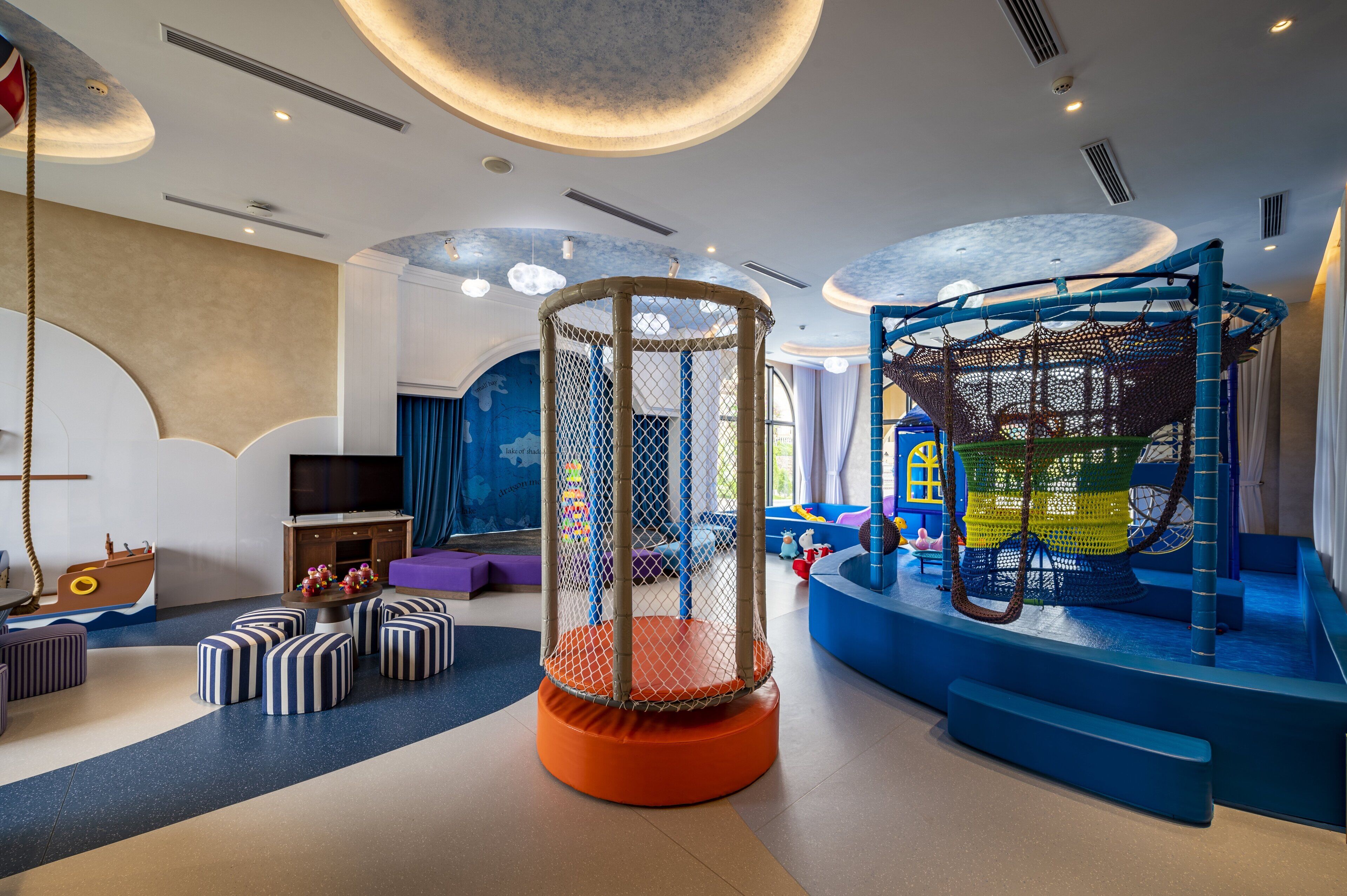 Un espace de jeux pour enfants avec une structure d’escalade en filet, un espace de jeux avec des éléments souples et un téléviseur dans un coin.