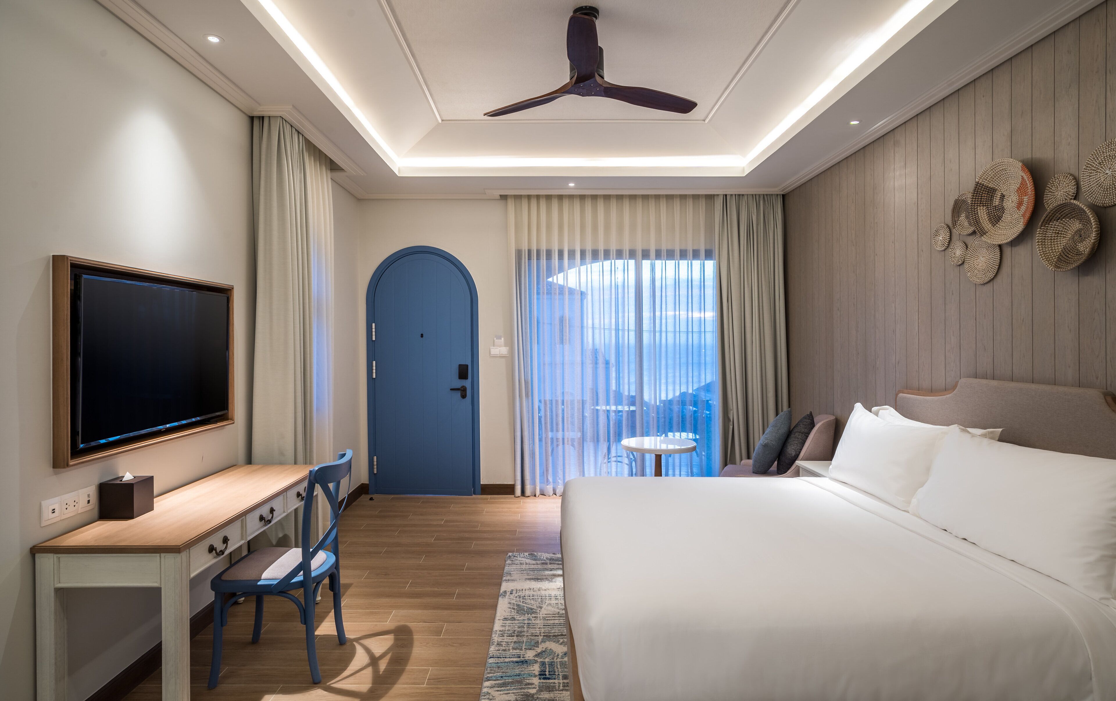 Habitación de hotel con cama, escritorio, silla, televisión y vistas al exterior a través de la ventana.