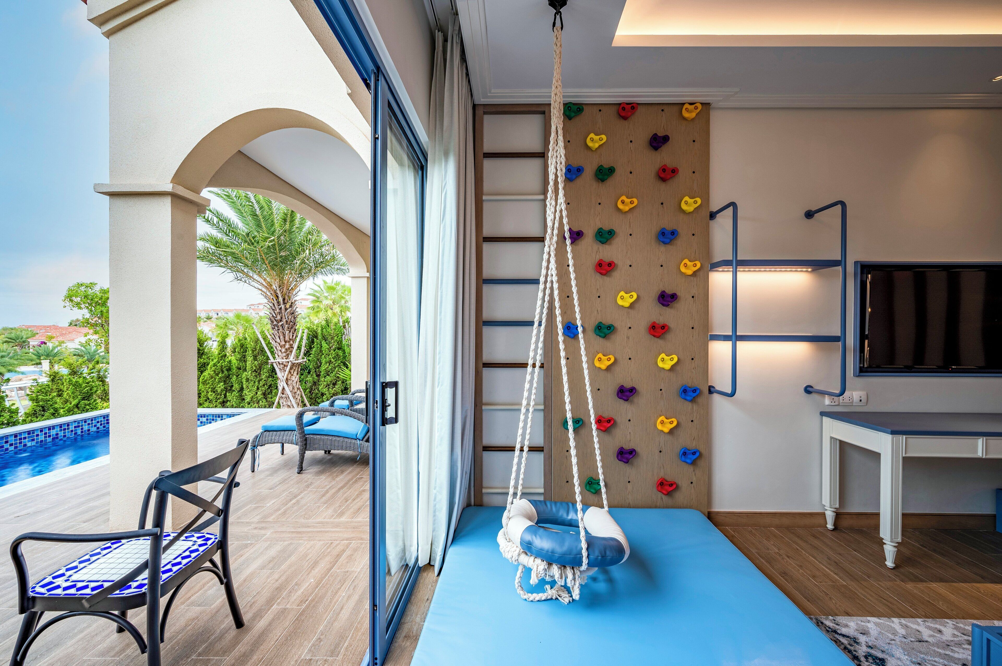 A room with a blue sofa, a hanging chair, a climbing wall, and a TV.
