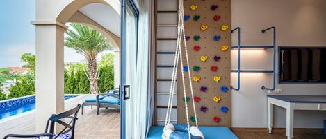 A room with a blue sofa, a hanging chair, a climbing wall, and a TV.