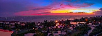 Un resort costero con vistas a la puesta de sol sobre el océano, palmeras y zonas de estar al aire libre.